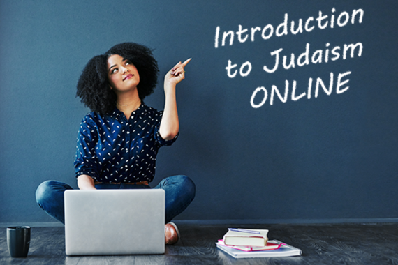 Woman sitting at laptop pointing to chalkboard that says Introduction to Judaism Online