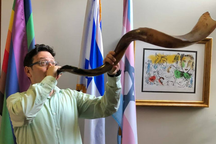 Rabbi Max Chaiken wears a green shirt and blows the shofar
