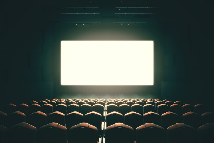 Dark and empty movie theater with a glowing white screen at the front of the room
