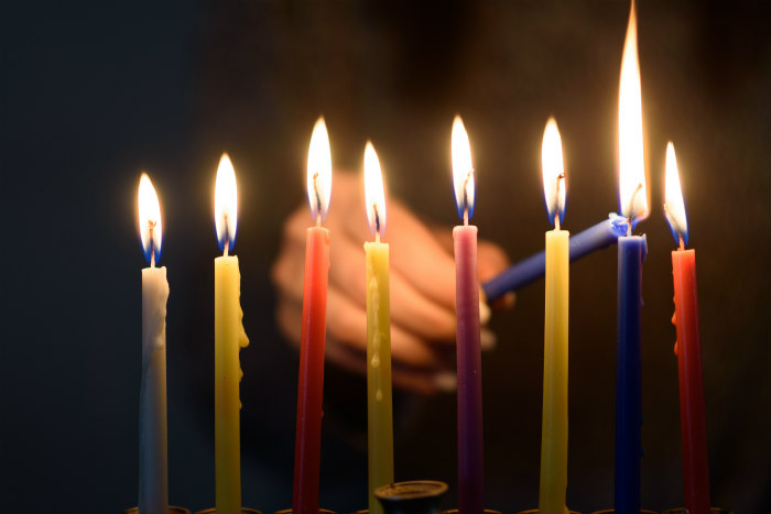 Hand lighting a full menorah of colorful Hanukkah candles