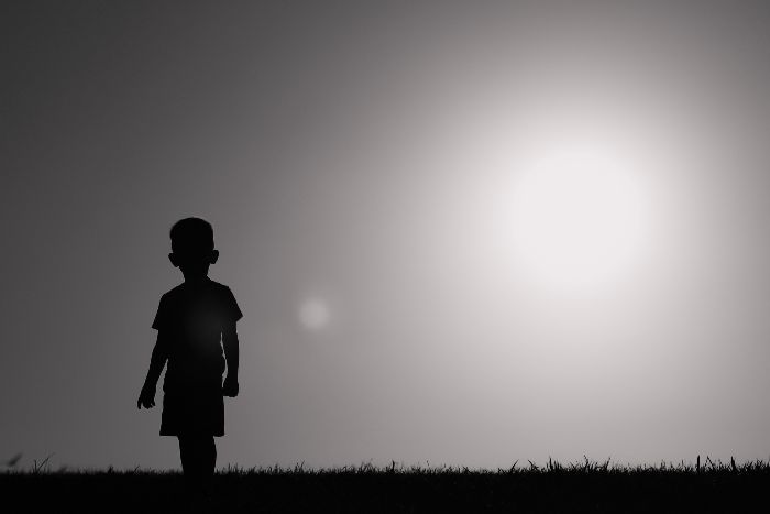 Silhouette of a young boy standing alone against a sunset