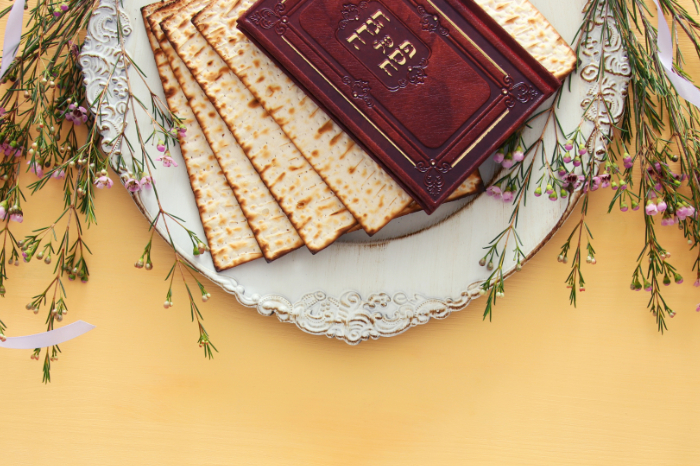 White platter with a stack of matzah and an old Haggadah on top all against a yellow table
