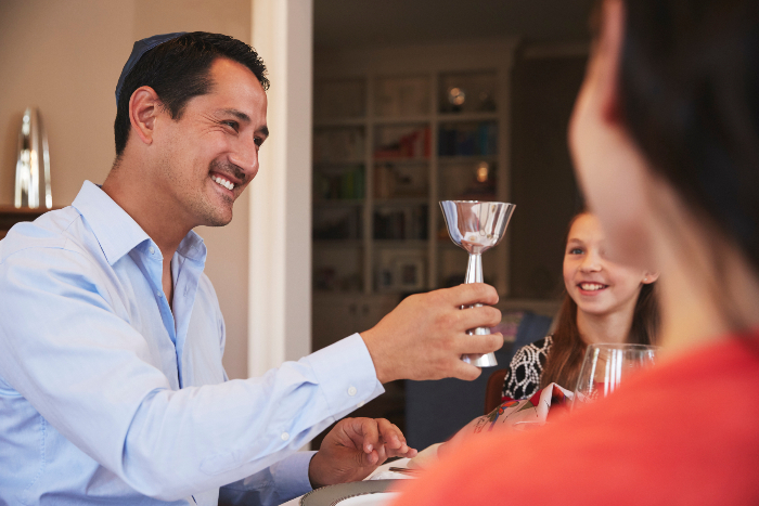 Father holding up a glass of wine at a family seder table