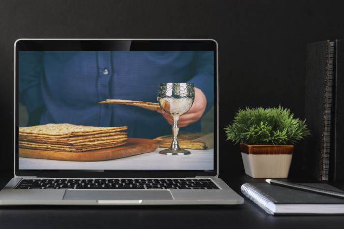 Laptop screen featuring a person sitting in front of a glass of wine and a pile of matzah