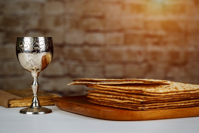 Pile of matzah atop a wooden platter next to a silver Kiddush cup 