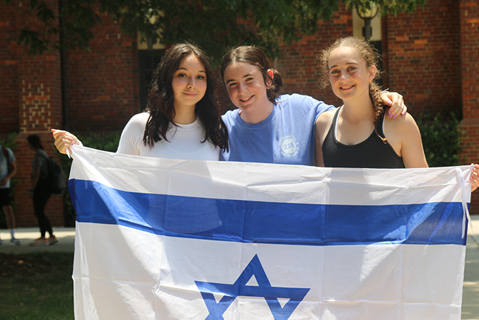 an image of three woman standing and holding an Israeli flag in front of them