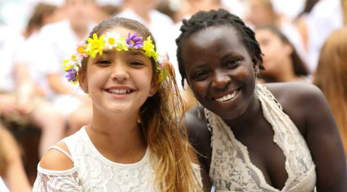 Two smiling young women wearing white lace dresses at an outdoor Shabbat service 