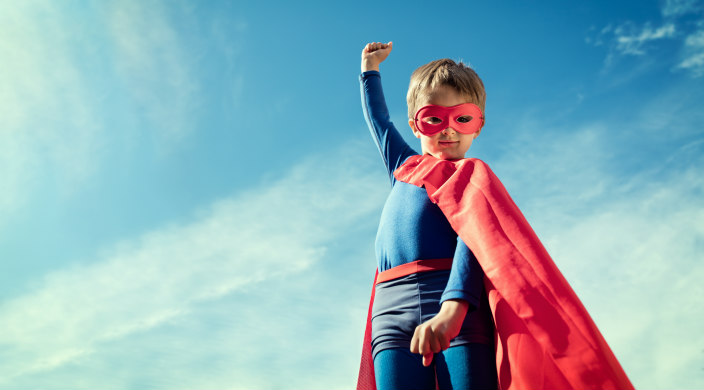 Child in a superhero costume with one fist raised against a blue sky background