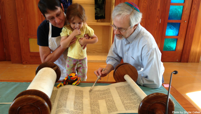 Rabbi, congregant and child look at a Torah scroll