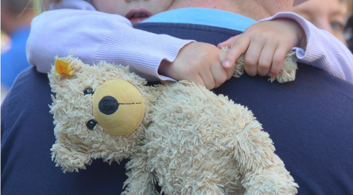 Little girl hugging her father while holding a teddy bear
