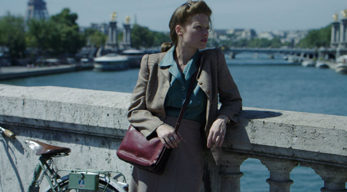 A woman in \WWII era dress stares out over a body of water