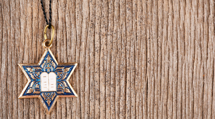 Colorful Jewish star and Ten Commandments charm on black cord suspended in front of light brown bark-like background