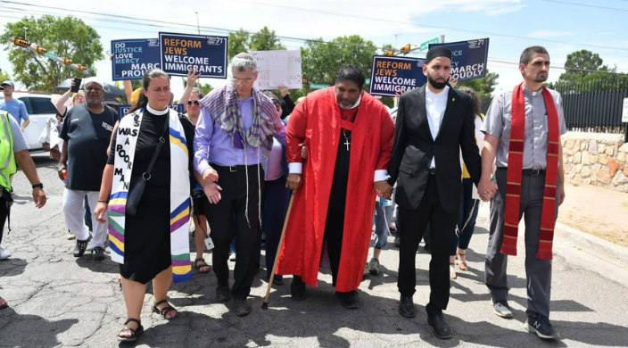 Interfaith leaders holding hands and marching for immigrant justice