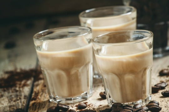 Beige liquid in three small shot glasses surrounded by coffee beans