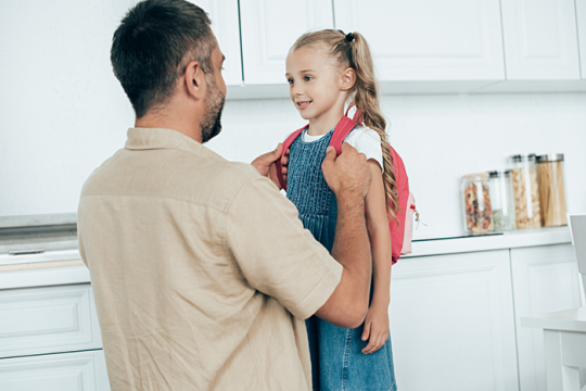 a smiling father and little daughter with backpack at home