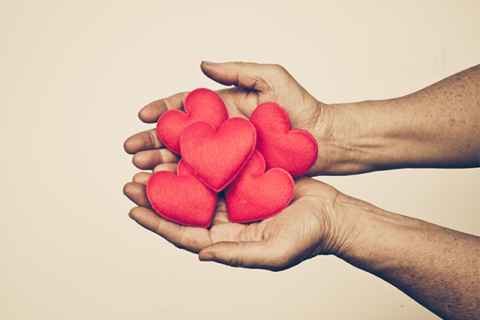Hands holding five cloth red hearts