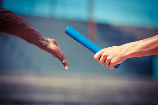 an image of one hand handing off the baton to another hand on a track field