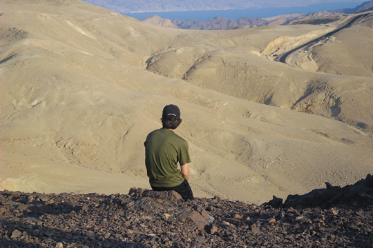 an image of a man sitting on a rock looking out into the desert