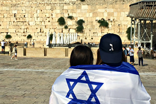 an image of two people wrapped in an Israeli flag looking at the Western Wall