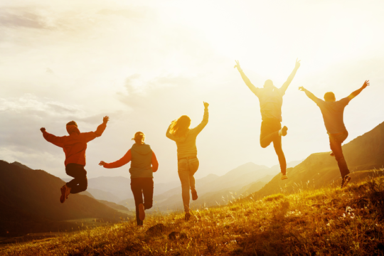 Photo of five people running and jumping on a hill with the sun shining behind them