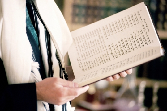 boy holding a Siddur, or a Jewish prayer book, to practice his beliefs and participate in a Jewish ritual.