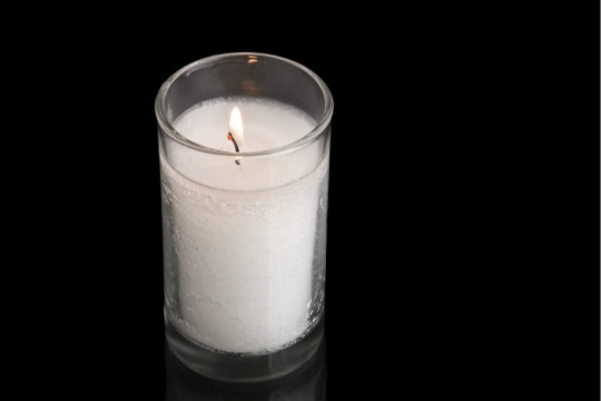 Unlit white memory candle in a glass votive against a black backdrop