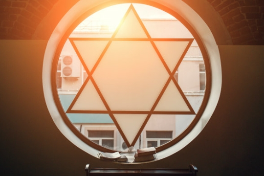 Circular stained glass window featuring a Star of David with open books sitting in the window sill