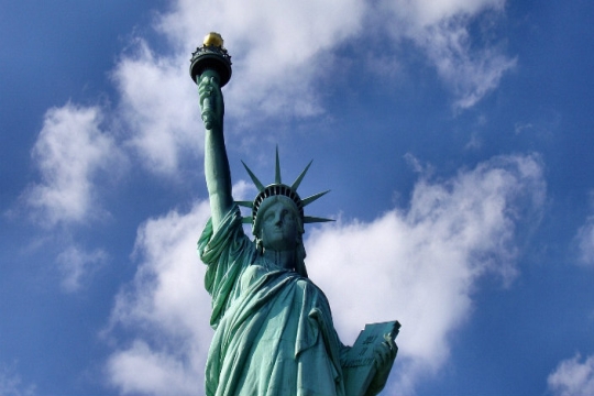 Closeup of the upper half of the Statue of Liberty against a blue sky with clouds