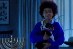 Screenshot from the video Puppy for Hanukkah of a child holding a puppy next to a Hanukkah menorah