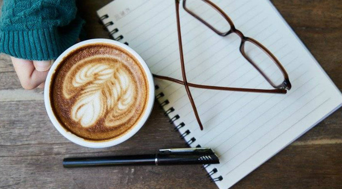 Womans hand holding a coffee cup next to a pen and a pad of paper
